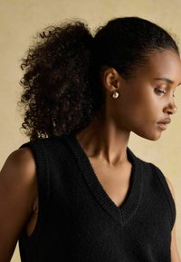 Czarna, bezrękawnikowa dzianinowa bluzka z dekoltem w kształcie litery V i teksturowanym wykończeniem, w połączeniu z okrągłymi złotymi kolczykami, akcentującymi gładkie metaliczne detale.