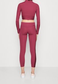 Burgundy kort topp och leggings-set gjort av stretchigt material. Har långa ärmar, åtsittande design och en mjuk yta.