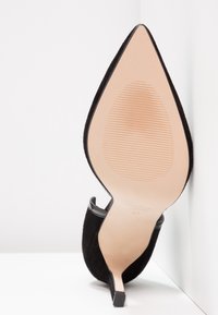 Chaussure à talon stiletto en daim noir avec un bout pointu et un talon fin. La semelle présente un motif texturé pour une meilleure adhérence. Taille 37.