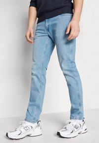 Jeans azzurri chiari in denim, a forma aderente, con dettagli di cucitura laterale. Abbinati a sneakers bianche con sottili accenti neri.