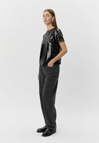 Sort glittertop med korte ærmer, parret med mørkegrå bukser med et diskret leopardmønster og sorte loafers.