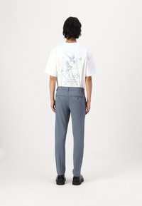 White graphic t-shirt with blue print featuring birds. Gray tapered trousers, smooth texture, with back pockets and a belt loop detail. Black shoes.