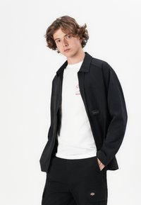 Chaqueta negra de corte relajado, combinada con una camiseta blanca con letras gráficas rojas y pantalones cargo negros.