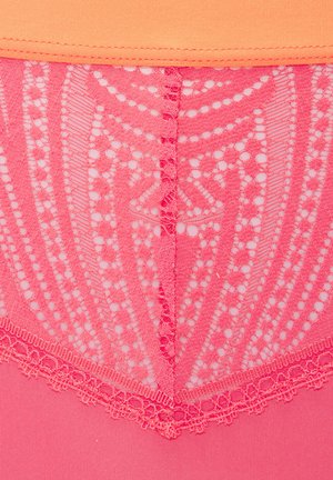 Close-up van roze kantstof met ingewikkelde bloem- en geometrische patronen boven op een effen roze materiaal, bedekt met een oranje band.