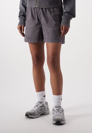 Grijze shorts met een gestructureerde afwerking, voorzien van zijzakken. Gecombineerd met witte sokken en grijze sportschoenen. Nadruk op functionaliteit en comfort.