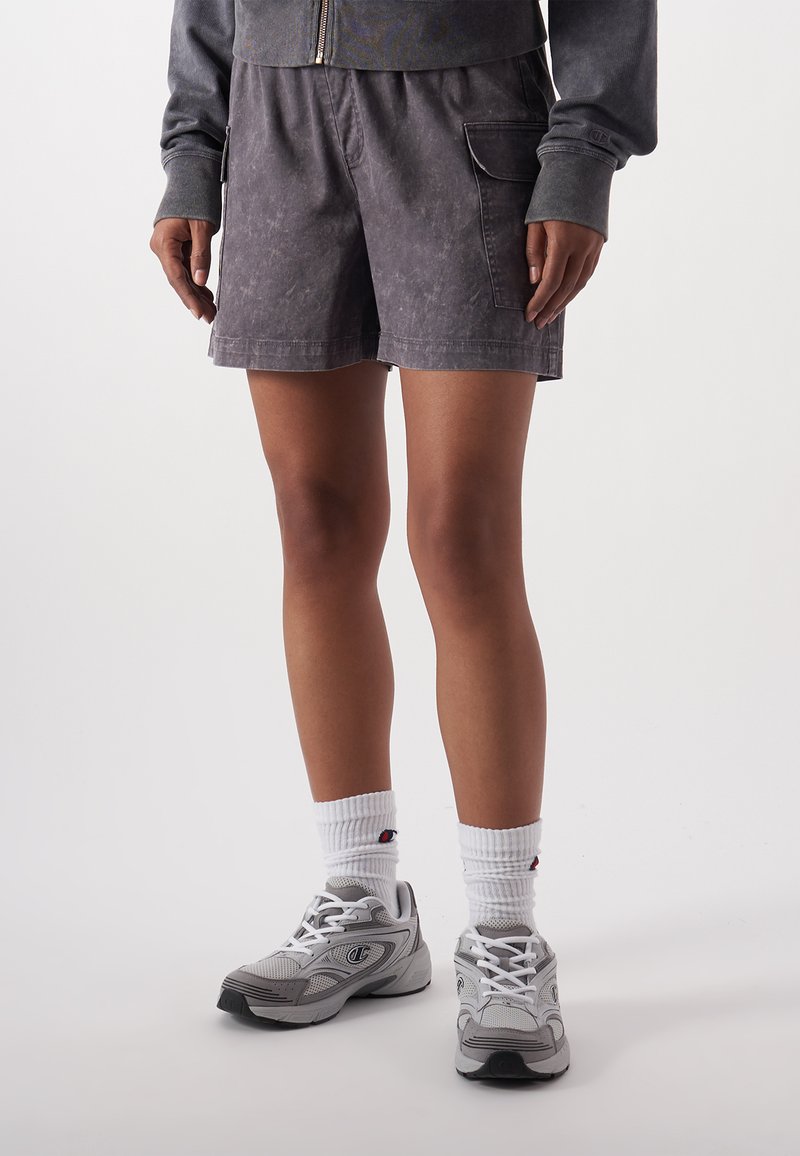 Graue Shorts mit einer strukturierten Oberfläche, ausgestattet mit Seitentaschen. Kombiniert mit weißen Socken und grauen Sportschuhen. Fokus auf Funktionalität und Komfort.