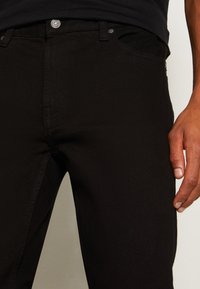 Svarta denimjeans med en slim fit, utrustade med knappstängning, bältesöglor och subtila sömnadsdetaljer. Tyget har en slät textur.