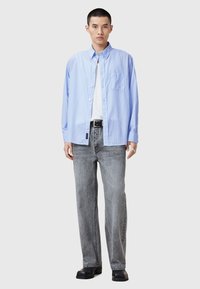 Blauwe gestreepte overhemd met lange mouwen en een borstzak, gedragen over een wit T-shirt en gecombineerd met grijze loszittende jeans en zwarte schoenen.