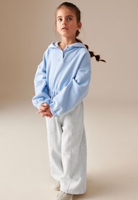 Lyseblå hoodie med en forhåndslomme og snoretræk, parret med grå brede sweats. Casual stof og afslappet pasform.