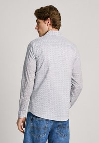 Långärmad skjorta i lätt tyg, med ett geometriskt mönster i blått och vitt. Knappar vid ärmsluten och en spetsig krage.