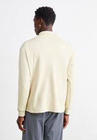 Lys beige langærmet polo shirt i tekstureret stof med klassisk krave, ribbede manchetter og et lille logo på den øvre ryg.