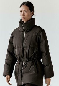 Kurtka puchowa w ciemnobrązowym kolorze, z wysokim kołnierzem, zamkiem błyskawicznym, talią ściąganą sznureczkami oraz elastycznymi mankietami. Gładka, pikowana tkanina.