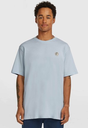 Lyseblå bomuld T-shirt med korte ærmer, rund halsudskæring, med en rund logo-patch på venstre brystområde og en afslappet pasform.