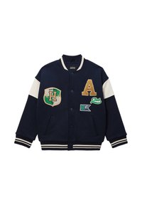 Veste varsity bleu marine avec des rayures blanches, ornée de patchs brodés, incluant la lettre 'A', un blason et des détails de logo.