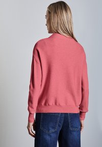 Pull en tricot rose avec un col rond, des poignets et un ourlet côtelés. Associé à un denim bleu foncé, mettant en avant une coupe décontractée et une texture douce.