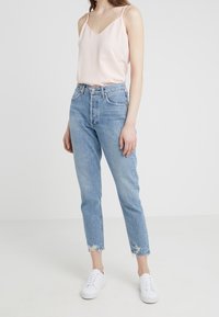 Světle růžová saténová košilka s výstřihem do V, kombinovaná s džíny z světlého denimu s vysokým pasem a roztrhanými lemy, doplněná bílými teniskami.