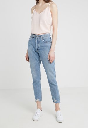 Camiseta de satén rosa claro con escote en V, combinada con unos vaqueros de mezclilla azul claro de talle alto con dobladillos deshilachados, complementados con zapatillas blancas.