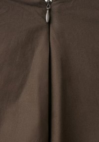 Primer plano de una cremallera marrón cerrada sobre tela, destacando el tirador metálico y los detalles de costura.