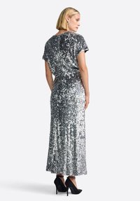 Sidabrinė suknelė su blizgučiais, trumpomis rankovėmis ir prigludusia juosmens linija, pereinanti į pilno ilgio sijoną. Suknelė derinama su juodais aukštakulniais bateliais.