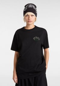 Black cotton t-shirt with short sleeves featuring green and white embroidered logo on the chest. Paired with a black knit beanie.