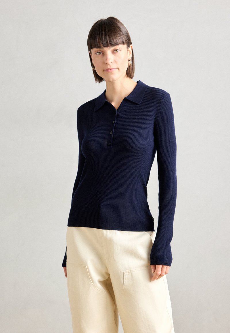 Pull à côtes bleu marine avec un col et une patte de boutonnage à cinq boutons. Dispose de manches longues et d'une fente latérale au niveau de l'ourlet.