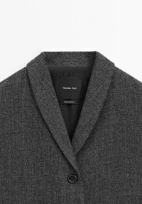 Czarna teksturowana marynarka z kołnierzem szalowym, jeden guzik z przodu oraz metka z napisem "Massimo Dutti" wewnątrz dekoltu.