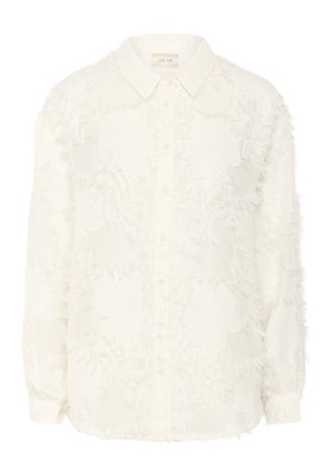 Bijela košulja s dugim rukavima izrađena od mekane, teksturirane tkanine s istrošenim uzorkom. Ima špicasti ovratnik.