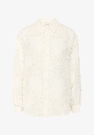 Chemise blanche à boutons en tissu doux et texturé, avec un motif effiloché. Elle a un col pointu et des manches longues.