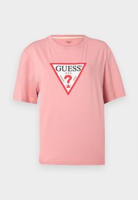 Camiseta de algodón de manga corta color rosa con un logo triangular rojo y blanco de Guess que dice "GUESS U.S.A. Washed Jeans" en el frente.