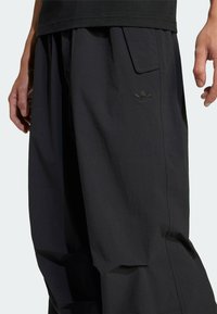 Černé pracovní kalhoty s volnějším střihem, vyrobené z texturované látky, s boční kapsou a jemným vyšívaným logem na stehně.