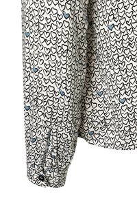 Weißes Hemd mit einem wiederholenden schwarzen Herzmuster und kleinen blauen Akzenten. Lange Ärmel mit Knopfdetails an den Manschetten. Weiche Stofftextur.