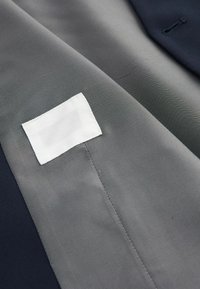 Gray textured fabric with a small white rectangular label stitched near the center, bordered by dark blue material.