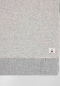 Felpa grigio chiaro con superficie testurizzata, orlo a costine grigio e etichetta bianca con grafiche rosse. Morbido materiale in misto cotone.