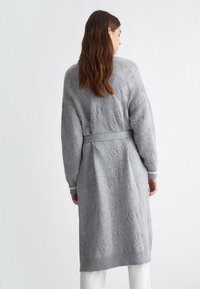 Lunga cardigan grigia lavorata a maglia con cintura, caratterizzata da un motivo testurizzato e polsini a costine. Strisce sottili sul fondo delle maniche.