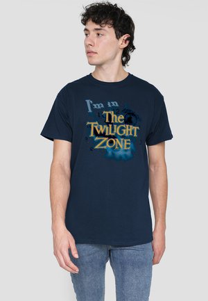 Navyblaue Baumwoll-T-Shirt mit einem grafischen Druck, der "Ich bin in der TWILIGHT ZONE" in Gelb- und Blautönen zeigt, vor einem dunkleren Hintergrund.