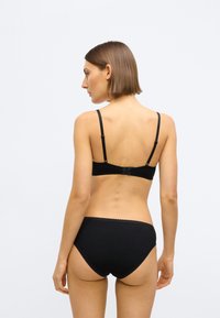 Soutien-gorge noir et slip assorti en tissu doux. Le soutien-gorge possède des bretelles fines réglables et une fermeture à agrafes, le slip a des bords festonnés.