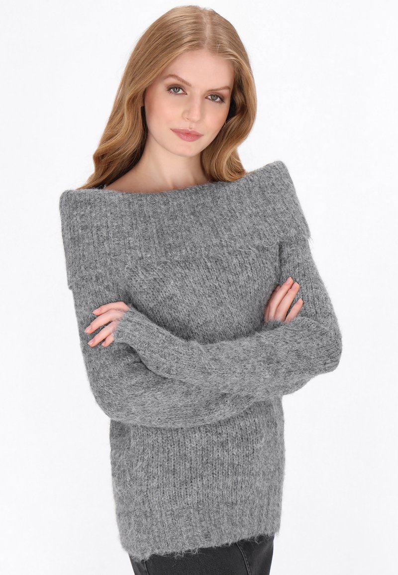 Világosszürke kötött pulóver laza, vállnál nyitott dekoltázssal, hosszú ujjakkal és texturált, bolyhos anyaggal. A dereknál szabott.