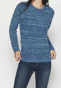 Pull en tricot bleu avec un motif texturé, col rond et manches longues. Le tissu semble duveteux et doux, avec des nuances de bleu variées.