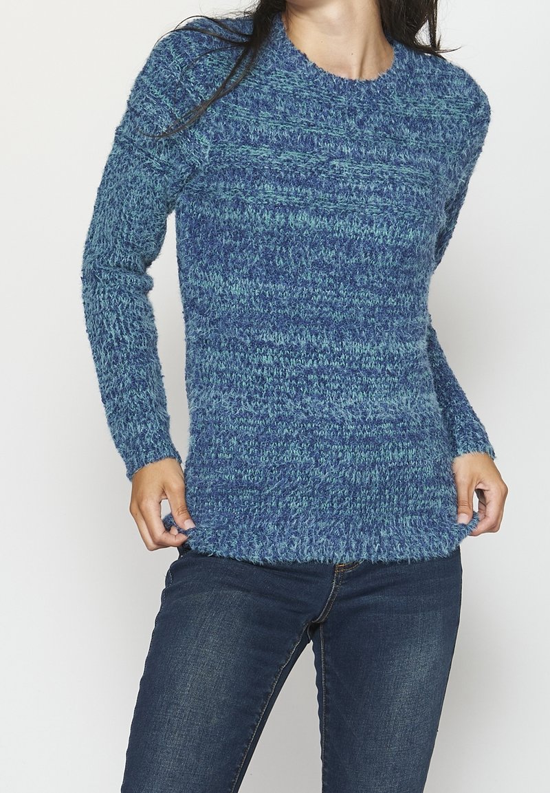 Pull en tricot bleu avec un motif texturé, col rond et manches longues. Le tissu semble duveteux et doux, avec des nuances de bleu variées.