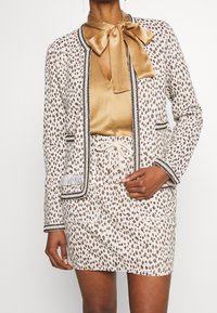 Jakardi printeinen bleiseri ja hame, jossa on sileä kultainen kauluskappi, mustat reunat ja tekstuuri, sivutaskut ja elastinen vyötärö.