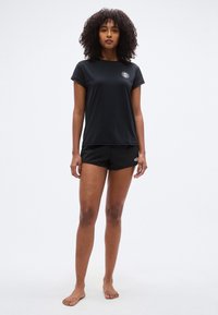 Μαύρο αθλητικό T-shirt με κοντά μανίκια και στρογγυλή λαιμόκοψη, συνδυασμένο με μαύρο σορτς. Διαθέτει κυκλικό λογότυπο στο στήθος.