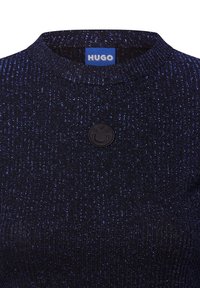 Schwarzes, geripptes Strickoberteil mit rundem Halsausschnitt und kleinem, strukturiertem, runden Logo-Patch mit "HUGO" auf der Vorderseite. Dezente, schimmernde Fäden.