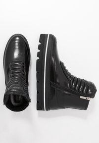 Botas de cuero negras hasta el tobillo con detalle acolchado, cremallera lateral y suela texturada con una franja blanca en una suela gruesa.