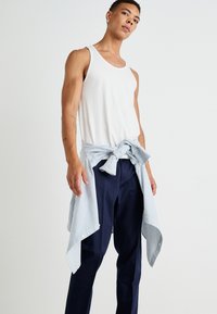Débardeur blanc sans manches, pantalon bleu marine et chemise à rayures bleu clair et blanche nouée autour de la taille ; coupe décontractée et tissu.