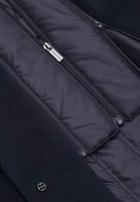 Ciemnogranatowa kurtka wykonana z miękkiego, strukturalnego materiału z pikowaną podszewką. Posiada dwa boczne zamki oraz zapięcie na guziki.