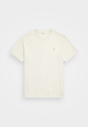 Krátky rukáv, krémové tričko vyrobené z bavlny, s malým vyšitým logom na ľavej dvore. Hladká textúra, okrúhly výstrih.
