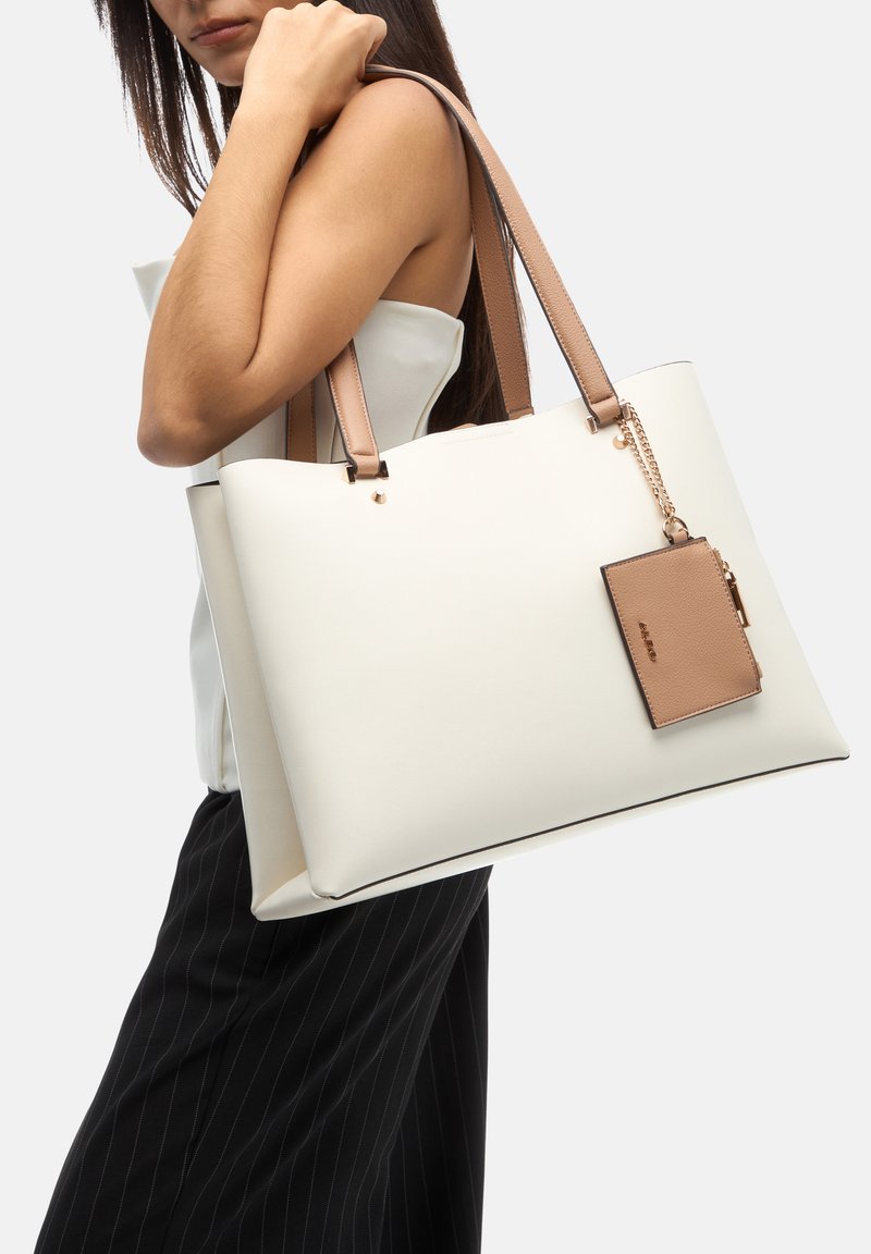 Borsa tote bianca con manici marrone chiaro, caratterizzata da una pochette rettangolare marrone attaccata da una catena e un design liscio e strutturato.