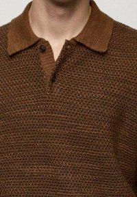 Hnědá texturovaná polo košile s pleteným vzorem, která má zapínání na knoflíky a kontrastní tmavší límec. Měkký povrch látky.