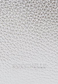 Pelle d'argento testurizzata con un motivo a croce, caratterizzata da un logo impresso "Coccinelle" nella parte inferiore.