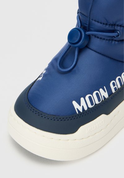 Jūras zila ūdensizturīga zābaku ar noapaļotu purngalu, teksturētu zoli, elastīgu aizdari ar pogu un baltu "MOON BOOT" zīmolu sānos.